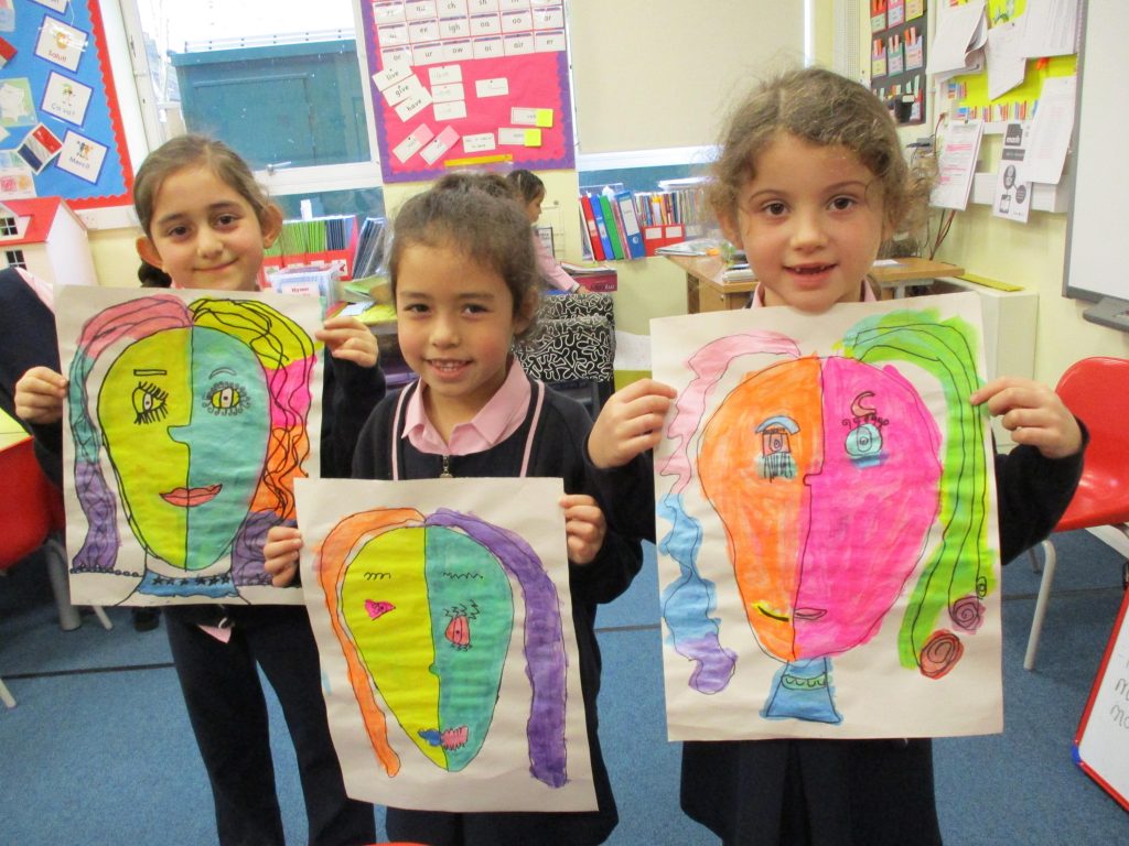 girls holding up coloured face drawings